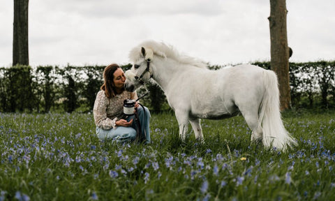Woman sitting in a field with a white horse