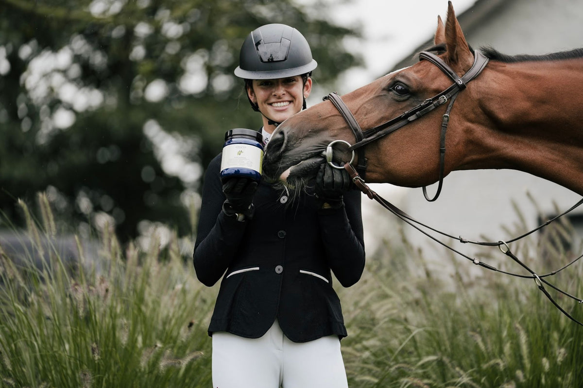 Smiling rider holding a Curafyt supplement pot while her horse nuzzles it